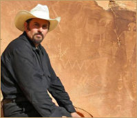 Portrait of Edward K Hudson, Artist and Oil Painter, wearing a cowboy hat, sitting in front of petroglyphs